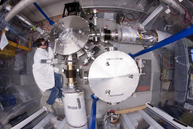 Vista de cima do Holometer enquanto um cientista do Fermilab trabalha no aparelho. O Holometer usa interferômetros gêmeos de laser para procurar o "ruído holográfico" no espaço-tempo e testar se o Universo é um holograma 2-D. Crédito: Fermilab.